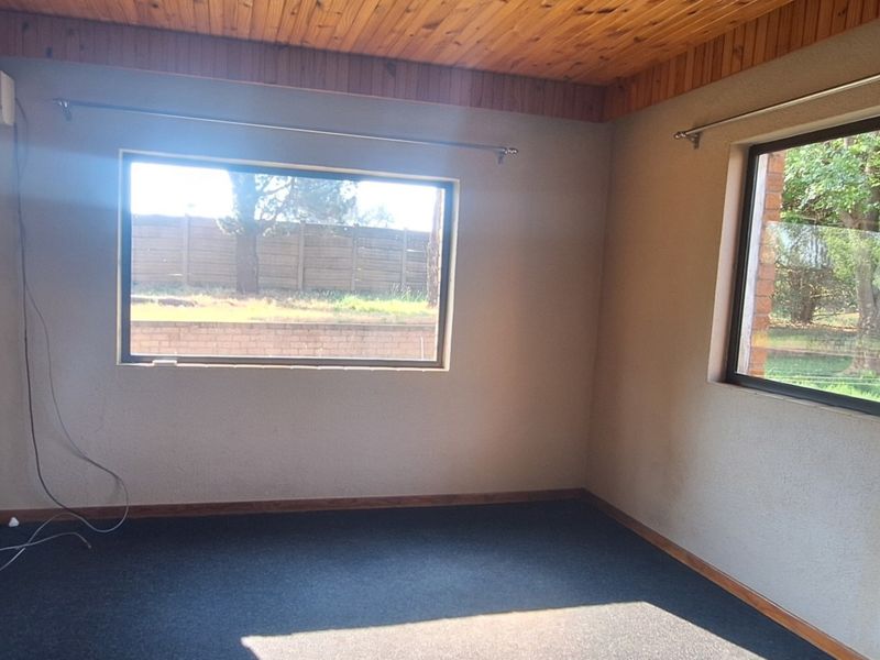 An empty bedroom featuring a timber-clad ceiling, carpeted flooring, and a wall-mounted air conditioning unit with views of the garden.