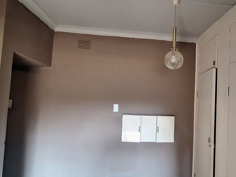 An empty bedroom featuring built-in cupboards, neutral wall paint, and a classic pendant light fixture, offering a blank canvas for renovation.
