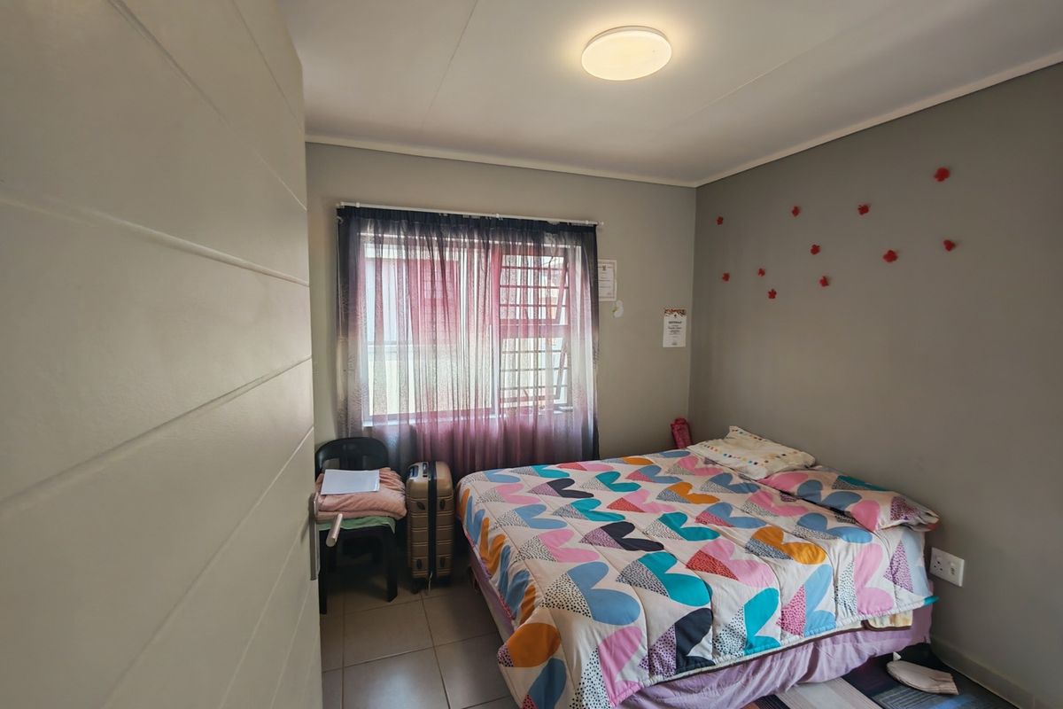 A functional bedroom featuring tiled flooring, security bars on the window, and neutral wall finishes, providing a practical living space.