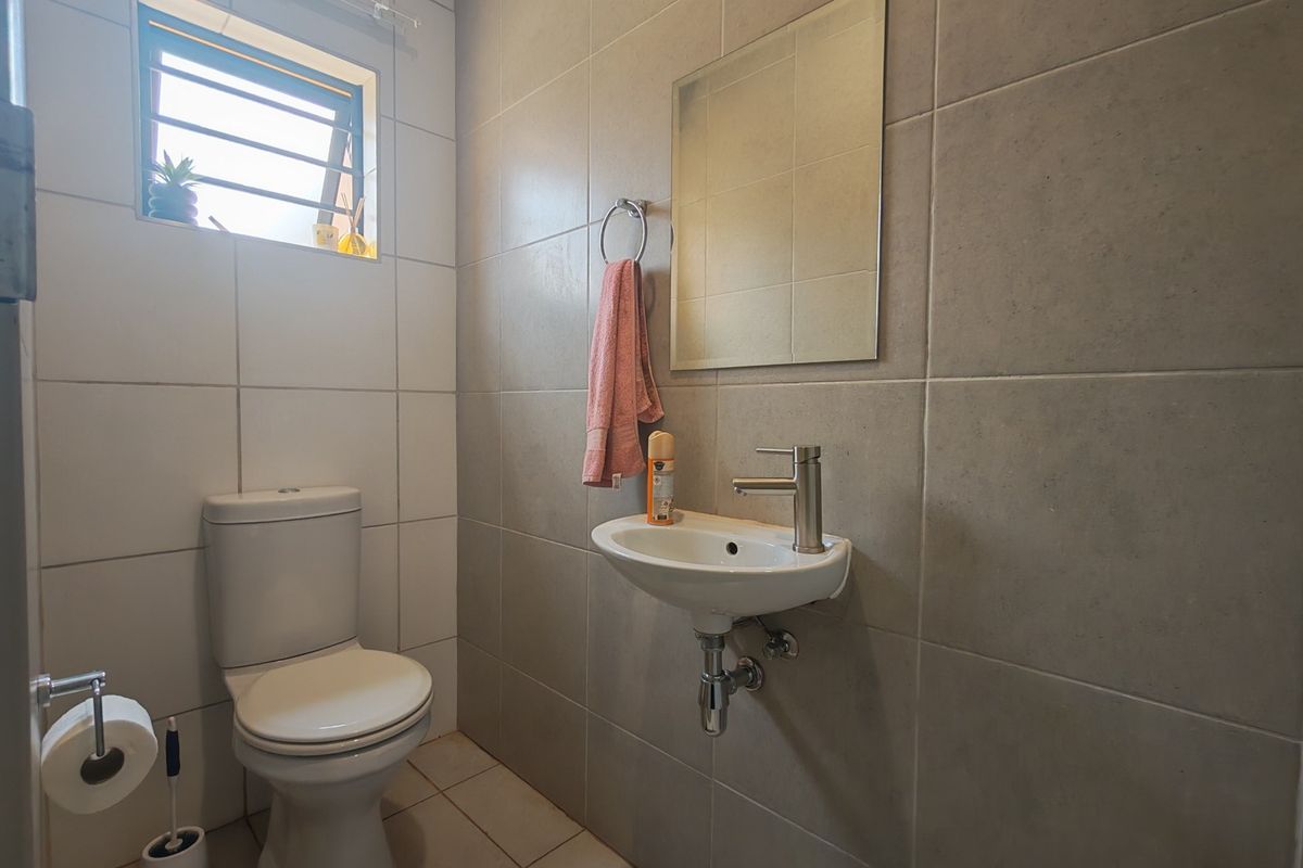 A compact, modern bathroom featuring neutral wall and floor tiles, a wall-mounted basin, and a standard toilet.