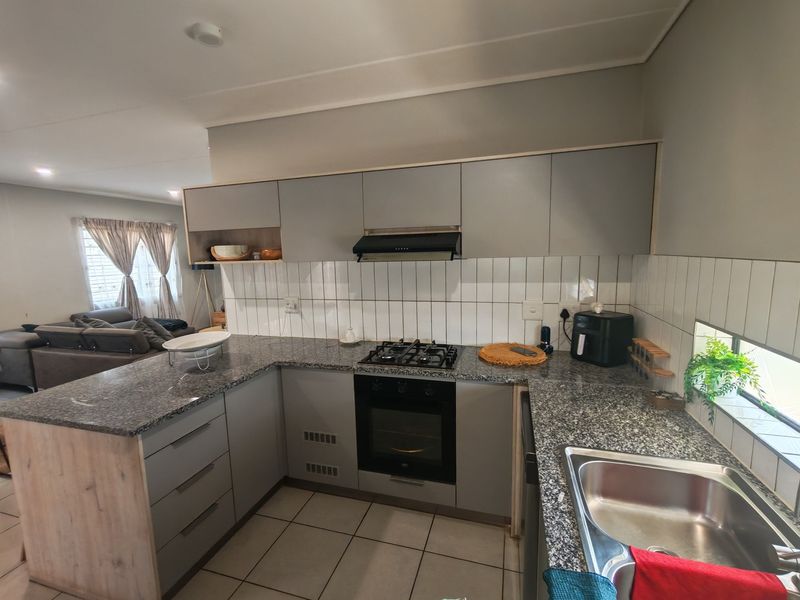 Modern kitchen featuring granite countertops, built-in oven, gas hob, extractor fan, and subway tile backsplash, seamlessly flowing into the adjacent living area.