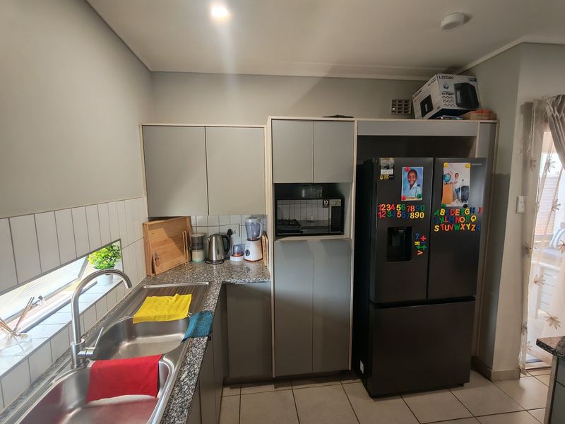 A functional kitchen featuring modern grey cabinetry, granite countertops, a stainless steel sink, and a built-in microwave, with tiled flooring and backsplash.