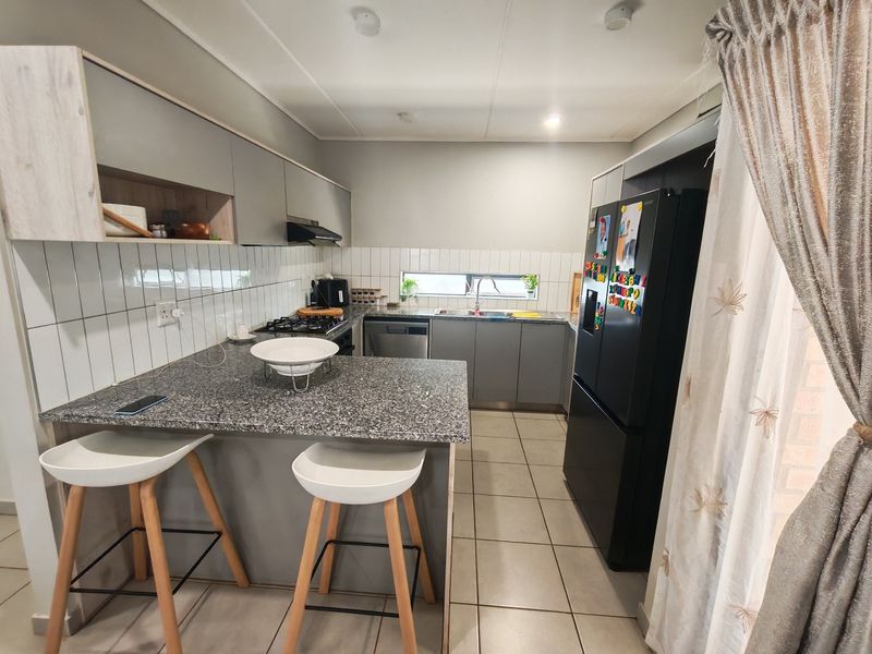 Modern kitchen featuring granite countertops, grey cabinetry, gas hob, extractor fan, and tiled backsplash with a breakfast bar area.