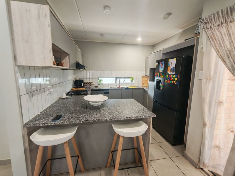 Modern kitchen featuring granite countertops, a breakfast bar, built-in cabinetry, gas hob, and tiled finishes, offering a functional and contemporary cooking space.