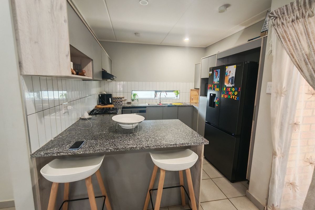 Modern kitchen featuring granite countertops, a breakfast bar, built-in cabinetry, gas hob, and tiled finishes, offering a functional and contemporary cooking space.