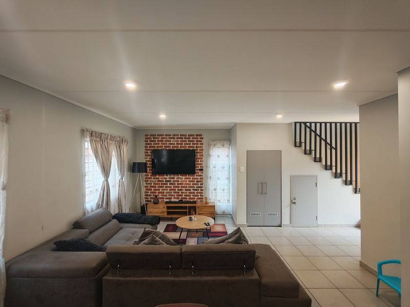 Spacious living room featuring an exposed brick feature wall, tiled flooring, recessed lighting, and an integrated staircase with a modern metal balustrade.