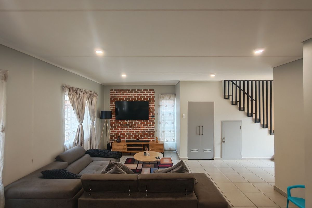 Spacious living room featuring an exposed brick feature wall, tiled flooring, recessed lighting, and an integrated staircase with a modern metal balustrade.
