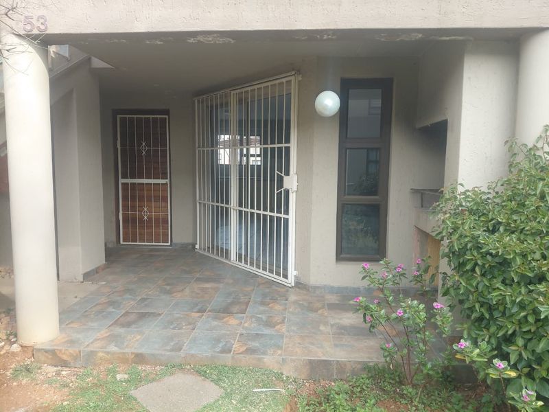Covered patio area featuring tiled flooring, a built-in braai, and security gates, providing a functional outdoor space for relaxation.