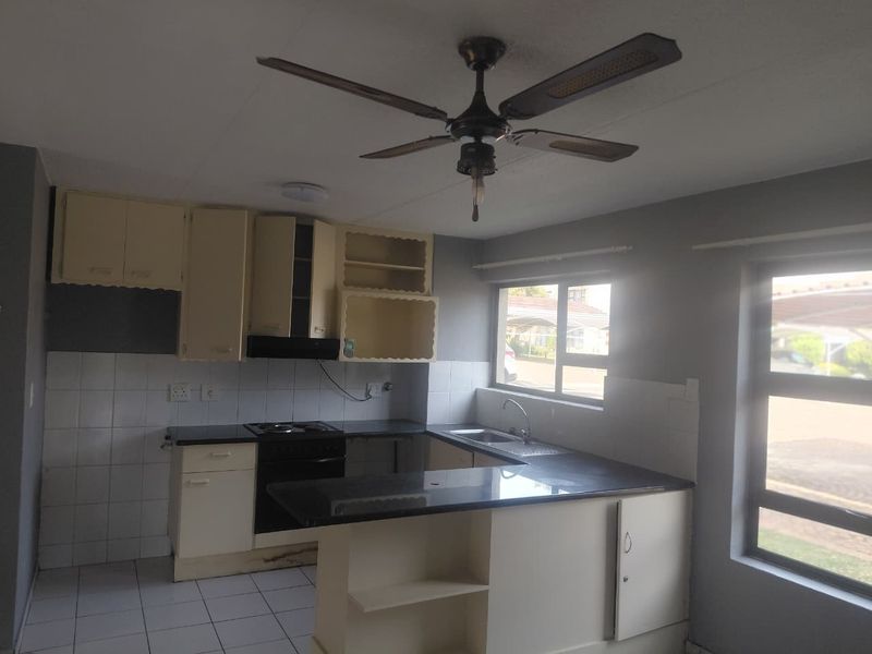 A functional kitchen featuring built-in cabinetry, a hob, oven, extractor fan, and a breakfast counter, with tiled flooring and backsplash throughout.
