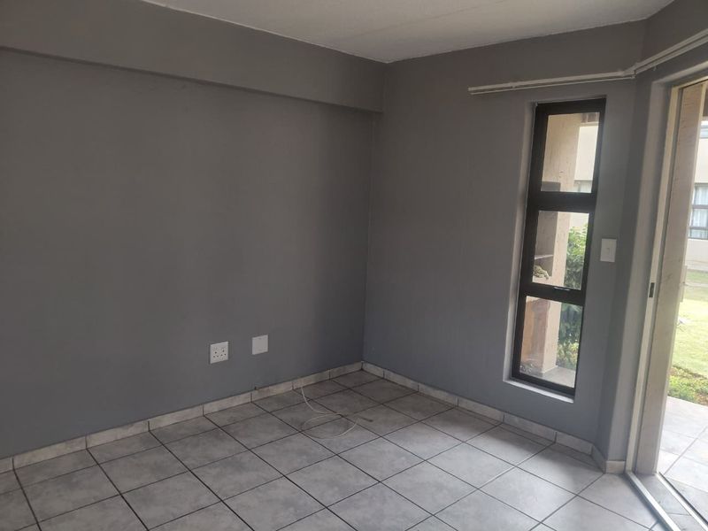An empty living room featuring grey painted walls, tiled flooring, and a sliding door providing access to an outdoor area.