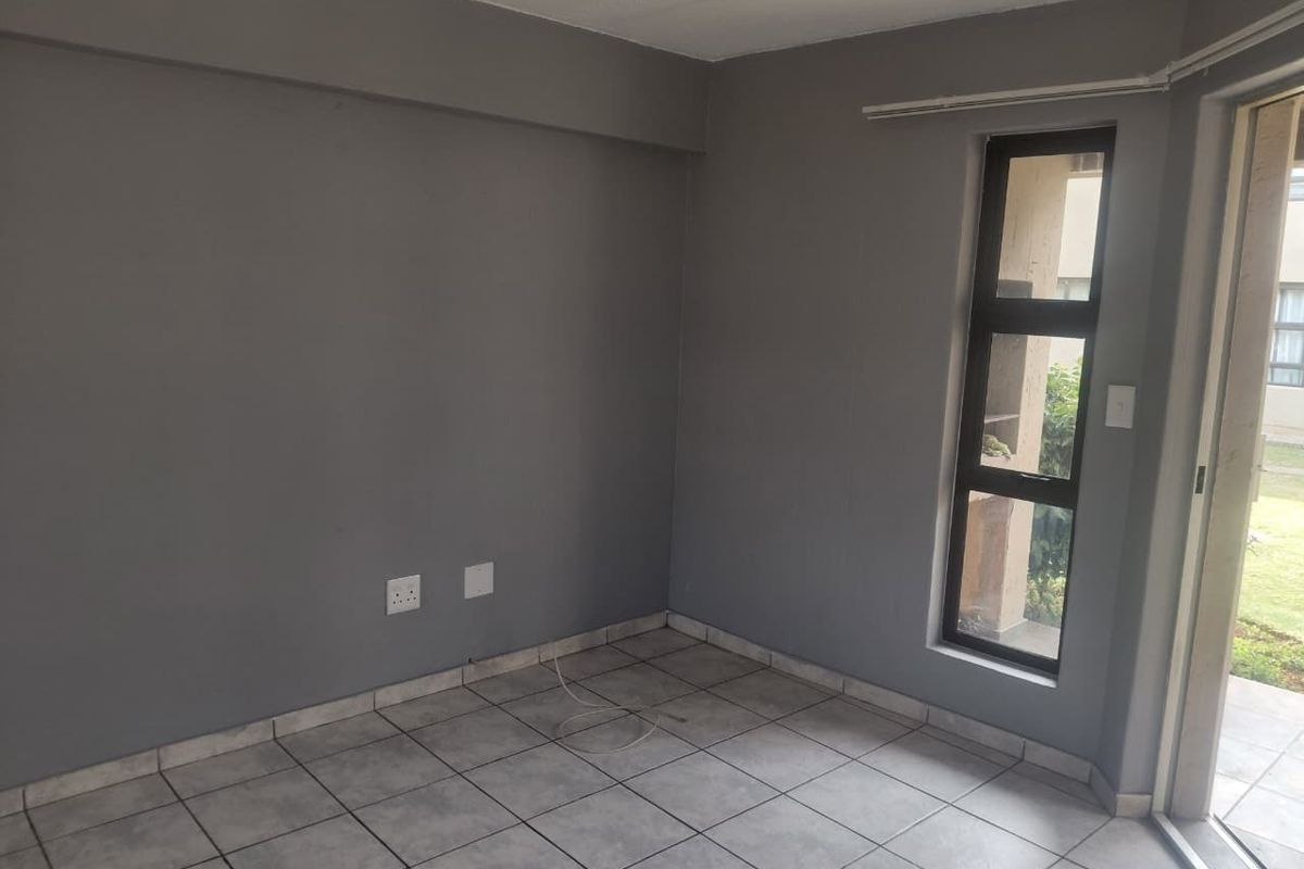 An empty living room featuring grey painted walls, tiled flooring, and a sliding door providing access to an outdoor area.
