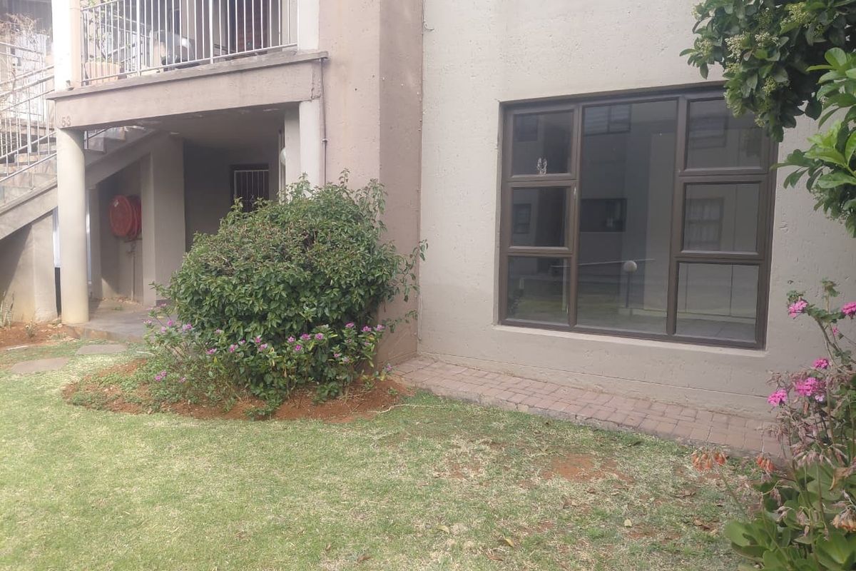 Ground floor apartment exterior featuring a small garden area, paved walkway, and a balcony above with metal railings.