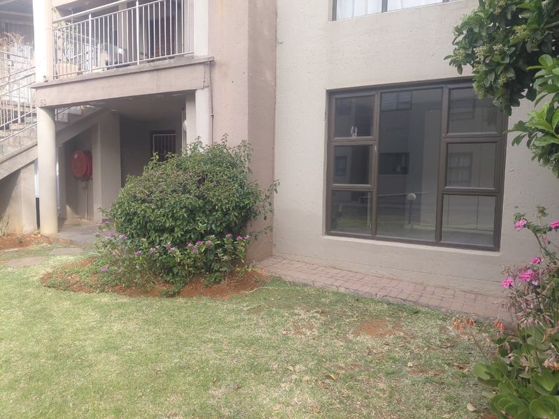 Ground floor apartment exterior featuring a small garden area, paved walkway, and a balcony above with metal railings.