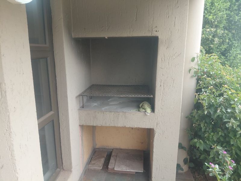 A built-in outdoor braai area on a patio, featuring a metal grill grate and lower storage space for firewood or accessories.