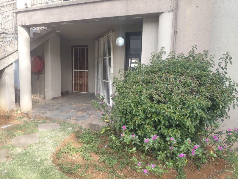Ground floor apartment entrance featuring a tiled patio, security gates, and a small garden area.