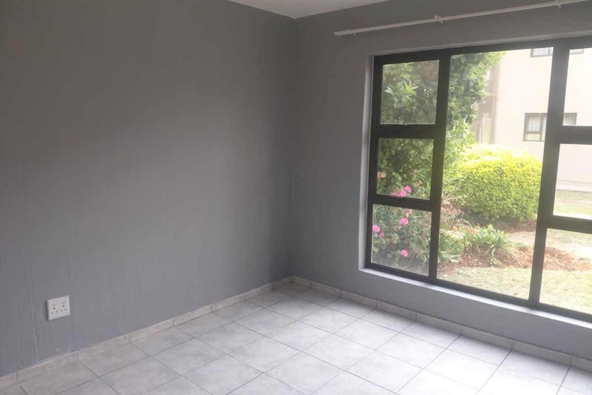 A bright, empty bedroom featuring neutral grey walls, tiled flooring, and a large window overlooking the garden.