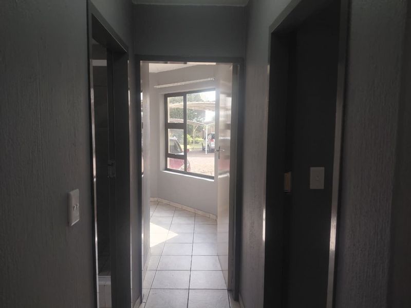 A functional hallway with tiled flooring leading towards an exterior window, providing access to adjacent rooms within the apartment.