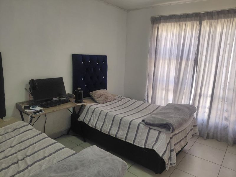 A functional bedroom featuring tiled flooring and a large sliding glass door with curtains, providing natural light to the space.