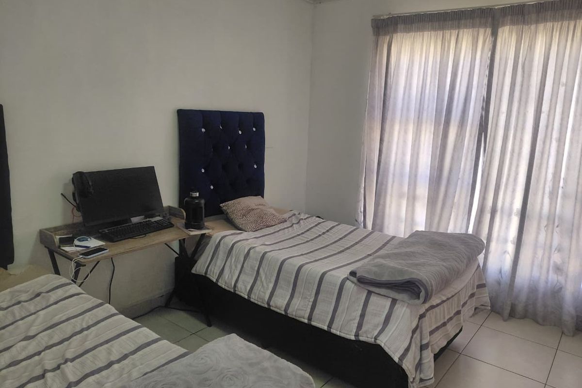 A functional bedroom featuring tiled flooring and a large sliding glass door with curtains, providing natural light to the space.