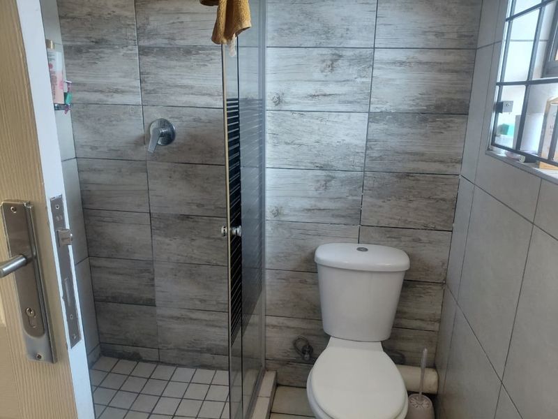 A compact bathroom featuring a glass-enclosed shower, a standard toilet, and modern wood-look wall tiling.