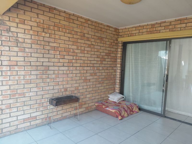 A covered patio area featuring exposed brick walls, tiled flooring, and a large sliding glass door providing access to the interior.
