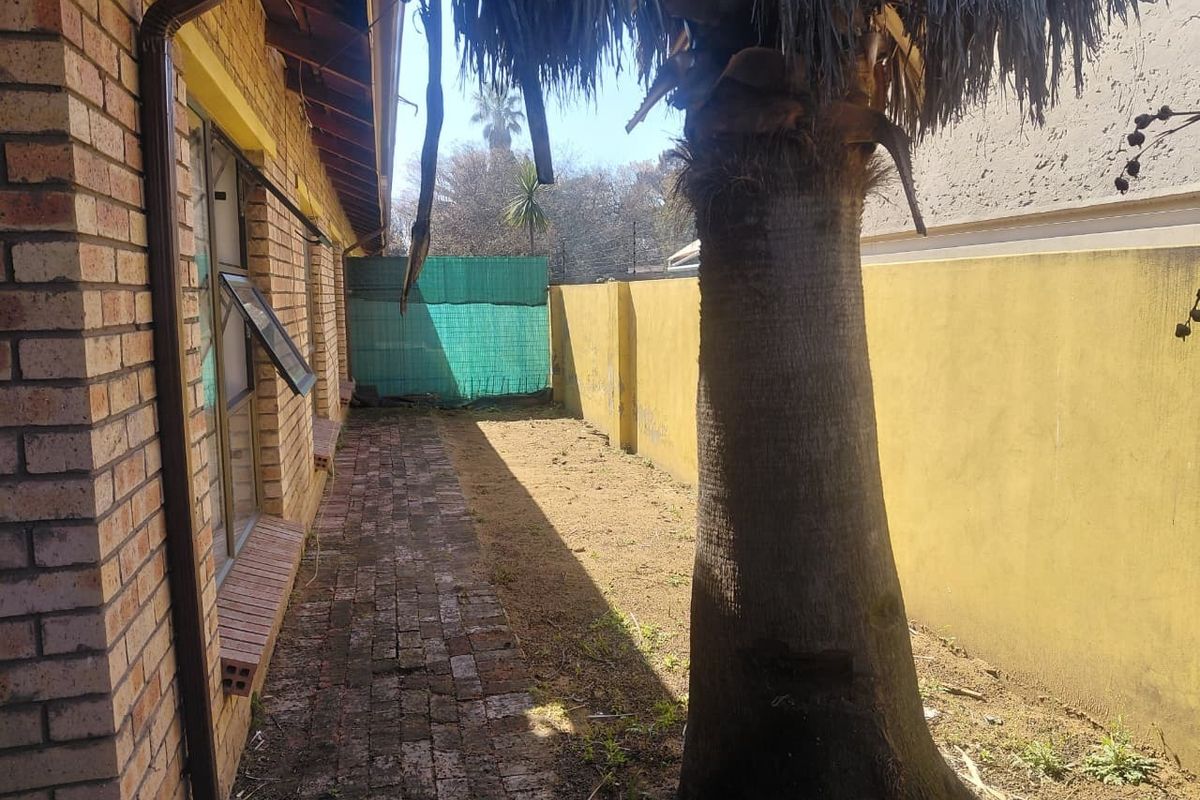 A rear exterior view of the townhouse featuring a brick-paved walkway, a boundary wall, and a mature palm tree in the garden area.