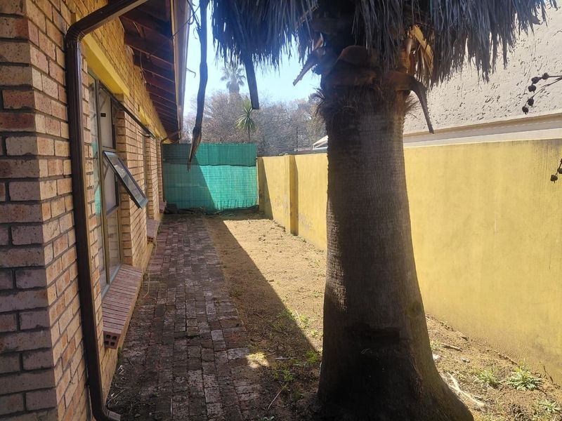 A rear exterior view of the townhouse featuring a brick-paved walkway, a boundary wall, and a mature palm tree in the garden area.