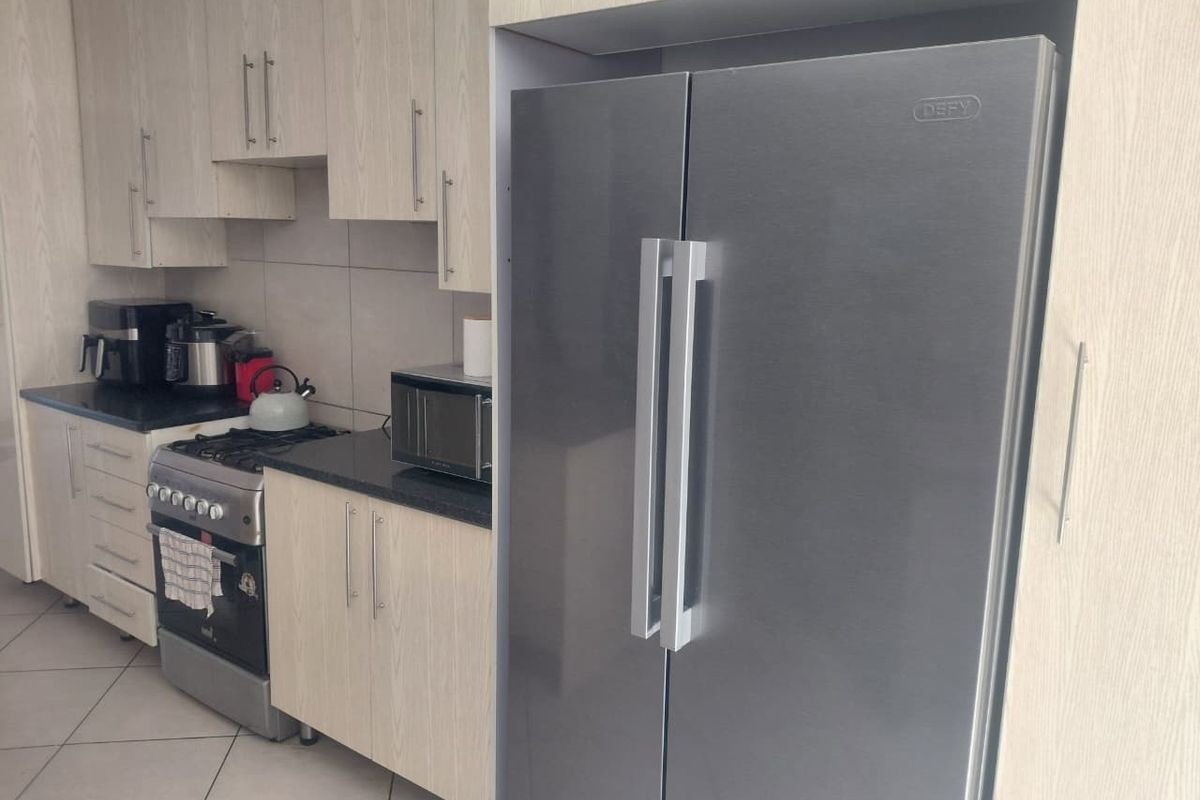 A functional kitchen featuring light wood-grain laminate cabinetry, dark granite countertops, tiled flooring, and a dedicated space for a large double-door refrigerator.