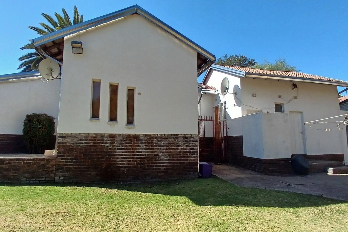 Rear view of the property featuring a brick and plaster facade, tiled roof, and a paved outdoor area leading to the garden.