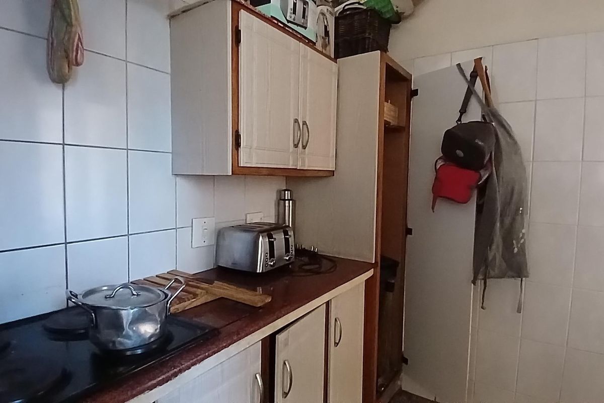 A compact kitchen area featuring built-in cabinetry, a tiled backsplash, and an integrated electric hob, showing signs of age and wear.