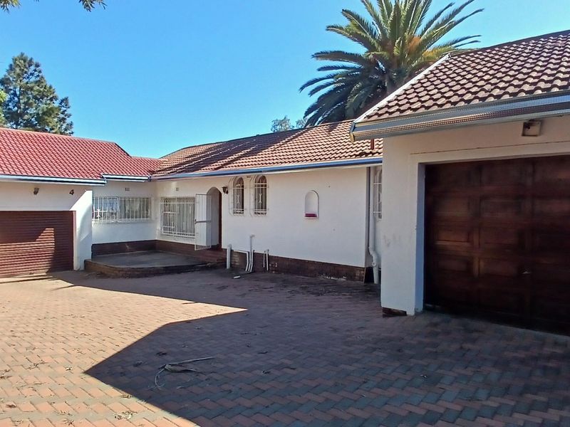 Front elevation of a single-story house featuring a paved driveway, multiple garage doors, and tiled roofing with security bars on windows.