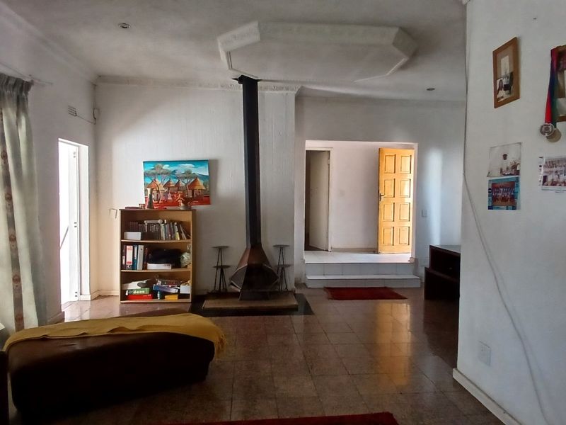 Living room featuring a central freestanding fireplace, tiled flooring, and a unique recessed ceiling detail, offering a functional space with potential for modernization.