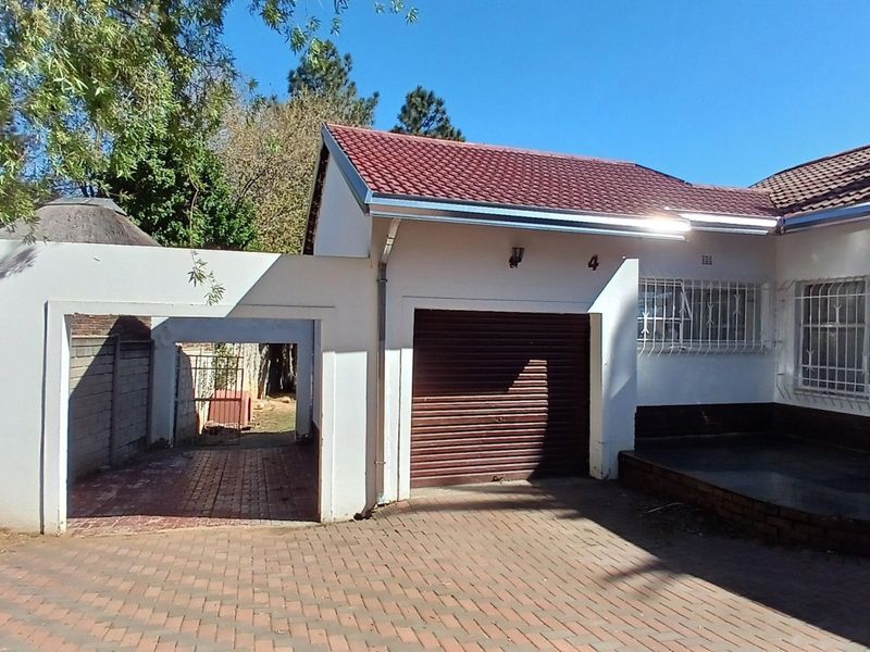 Front exterior view of the property featuring a paved driveway, a single garage with a roller shutter door, and an attached carport.