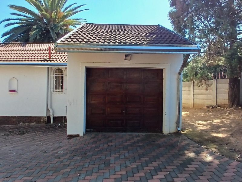 A detached single garage featuring a wooden door, tiled roof, and paved driveway, situated on a residential property with perimeter walling.