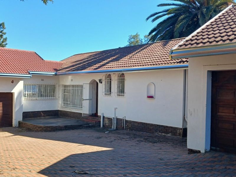 Front elevation of a single-story house featuring a paved driveway, multiple garage access points, and security-fitted windows under a tiled roof.