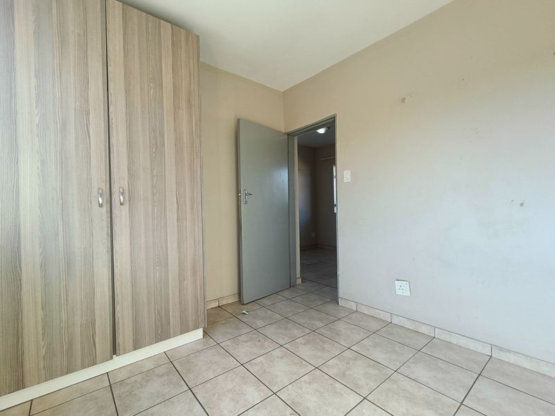 A vacant bedroom featuring neutral tiled flooring and a built-in wooden wardrobe, offering a clean canvas for personalization.