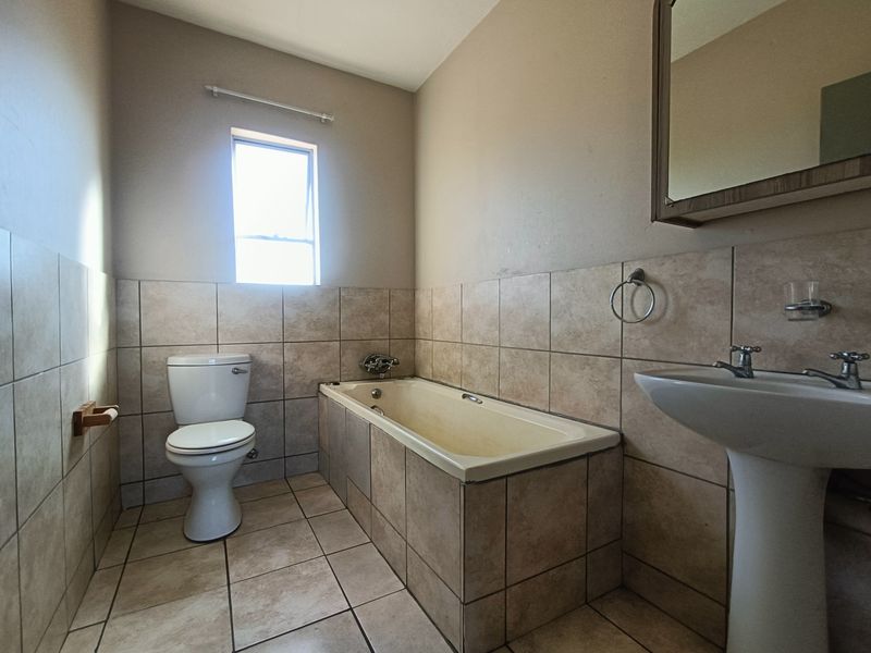 A functional bathroom featuring a pedestal basin, built-in bathtub, and toilet with neutral tiled finishes throughout.