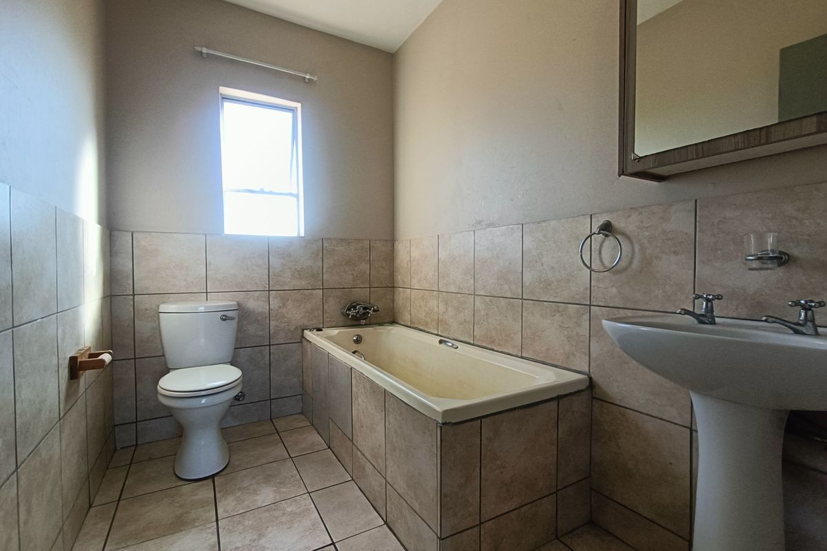 A functional bathroom featuring a pedestal basin, built-in bathtub, and toilet with neutral tiled finishes throughout.
