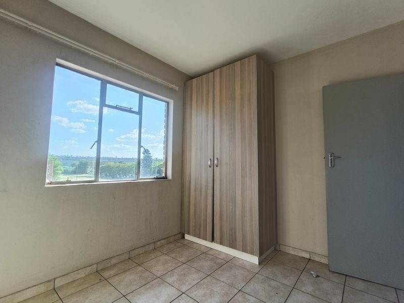 A vacant bedroom featuring tiled flooring, a built-in wooden wardrobe, and a window offering natural light and exterior views.