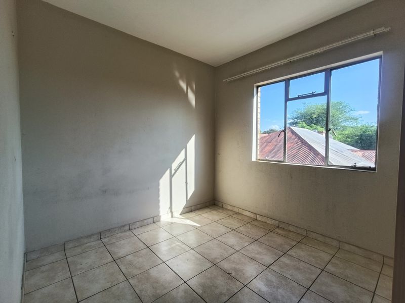 An empty bedroom featuring tiled flooring and a large window with an aluminium frame, offering a blank canvas for potential interior design.
