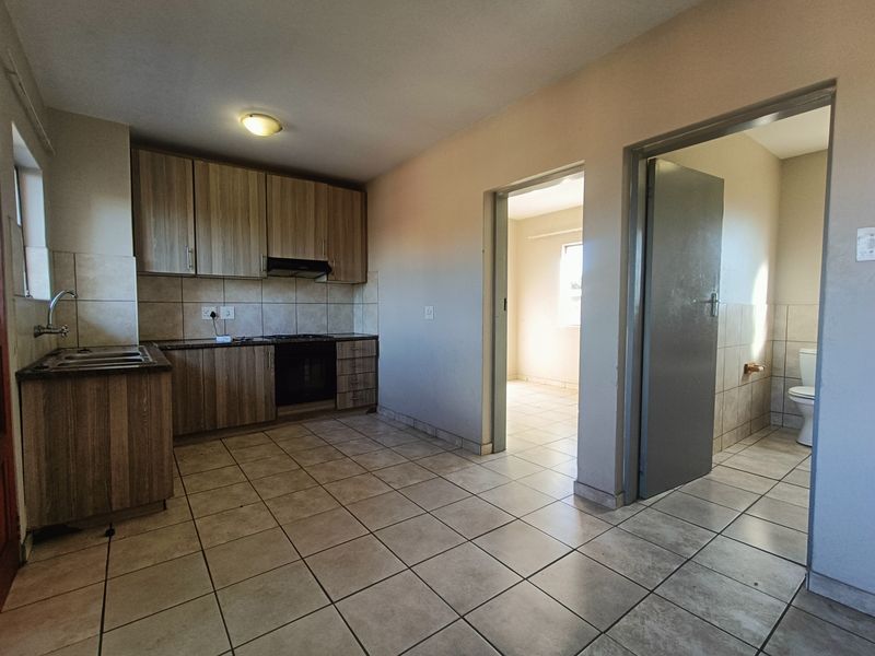 Open plan kitchen area featuring wood-look cabinetry, built-in oven, and tiled flooring, with direct access to adjacent rooms.