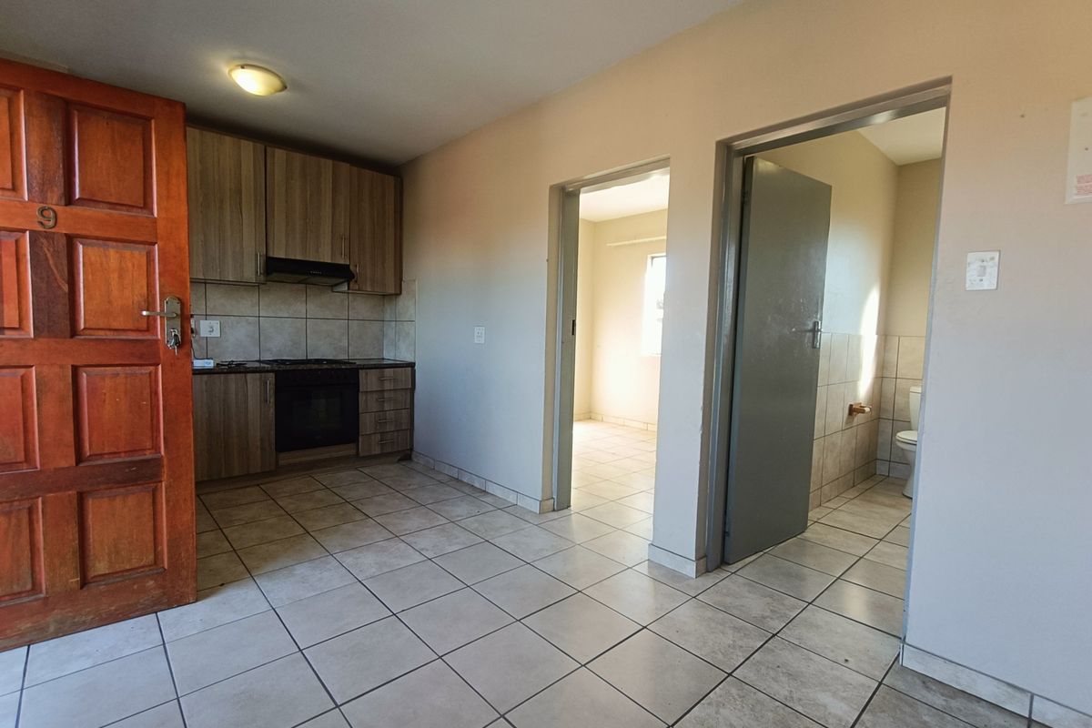 Open-plan living area featuring tiled flooring, built-in kitchen cabinetry with integrated oven and hob, and access to adjacent bedroom and bathroom.