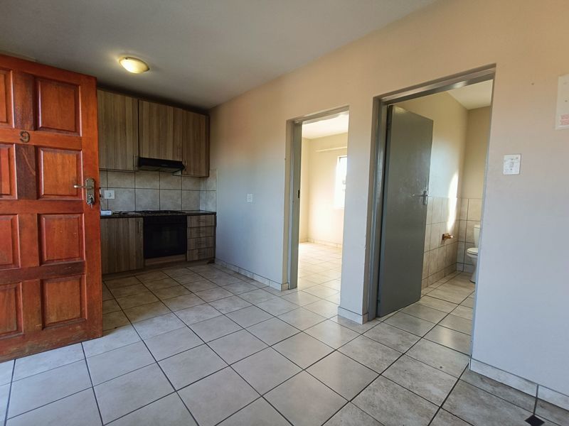 Open-plan living area featuring tiled flooring, built-in kitchen cabinetry with integrated oven and hob, and access to adjacent bedroom and bathroom.