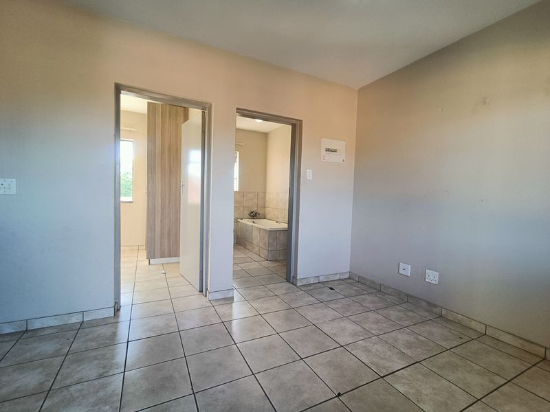 An empty bedroom featuring tiled flooring and direct access to an en-suite bathroom, providing a neutral canvas for personalization.
