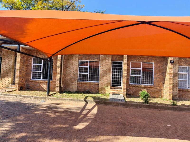 Front exterior view of a face brick townhouse featuring a paved driveway, security bars on windows, and a large orange shade sail carport.