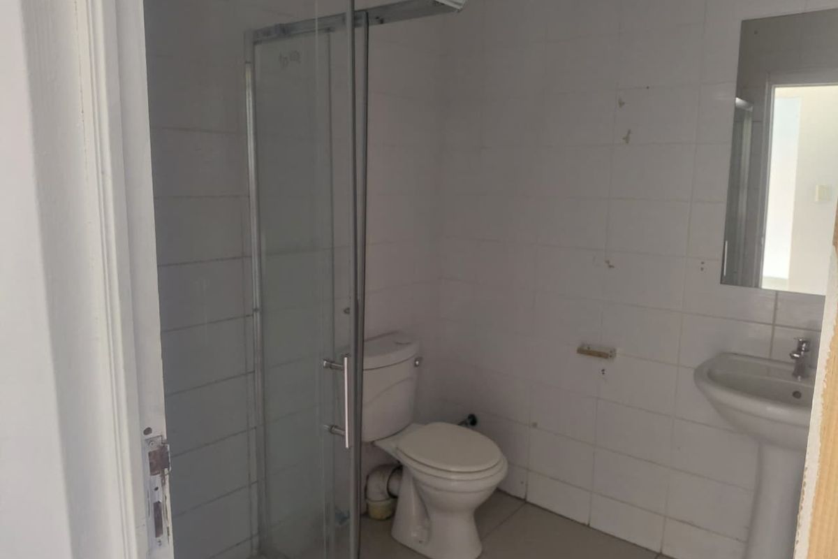 A functional bathroom featuring a shower enclosure, pedestal basin, and toilet, requiring cosmetic updates to the wall finishes.