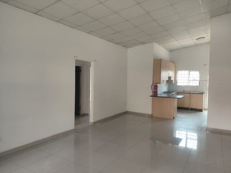 Open plan living area featuring tiled floors and a compact kitchen with built-in cabinetry, hob, and extractor fan.