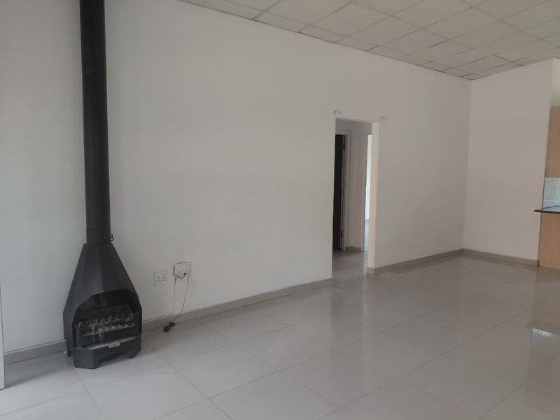 Spacious open-plan living area featuring tiled flooring, a freestanding fireplace, and a drop ceiling, offering a blank canvas for interior design.
