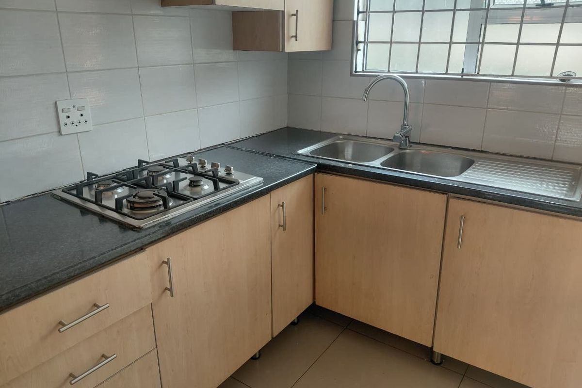A functional kitchen featuring light wood-look cabinetry, dark granite countertops, a gas hob, and a double stainless steel sink with tiled splashbacks.