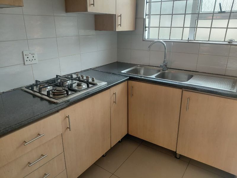 A functional kitchen featuring light wood-look cabinetry, dark granite countertops, a gas hob, and a double stainless steel sink with tiled splashbacks.
